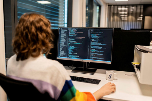 En utvikler ser på koden siden. På PC-skjermen er det tre kolonner med en rekke kodelinjer med ulike farger og innrykk.