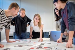 To mannlige og tre kvinnelige studenter jobber med utklipp fra magasiner rundt et bord.