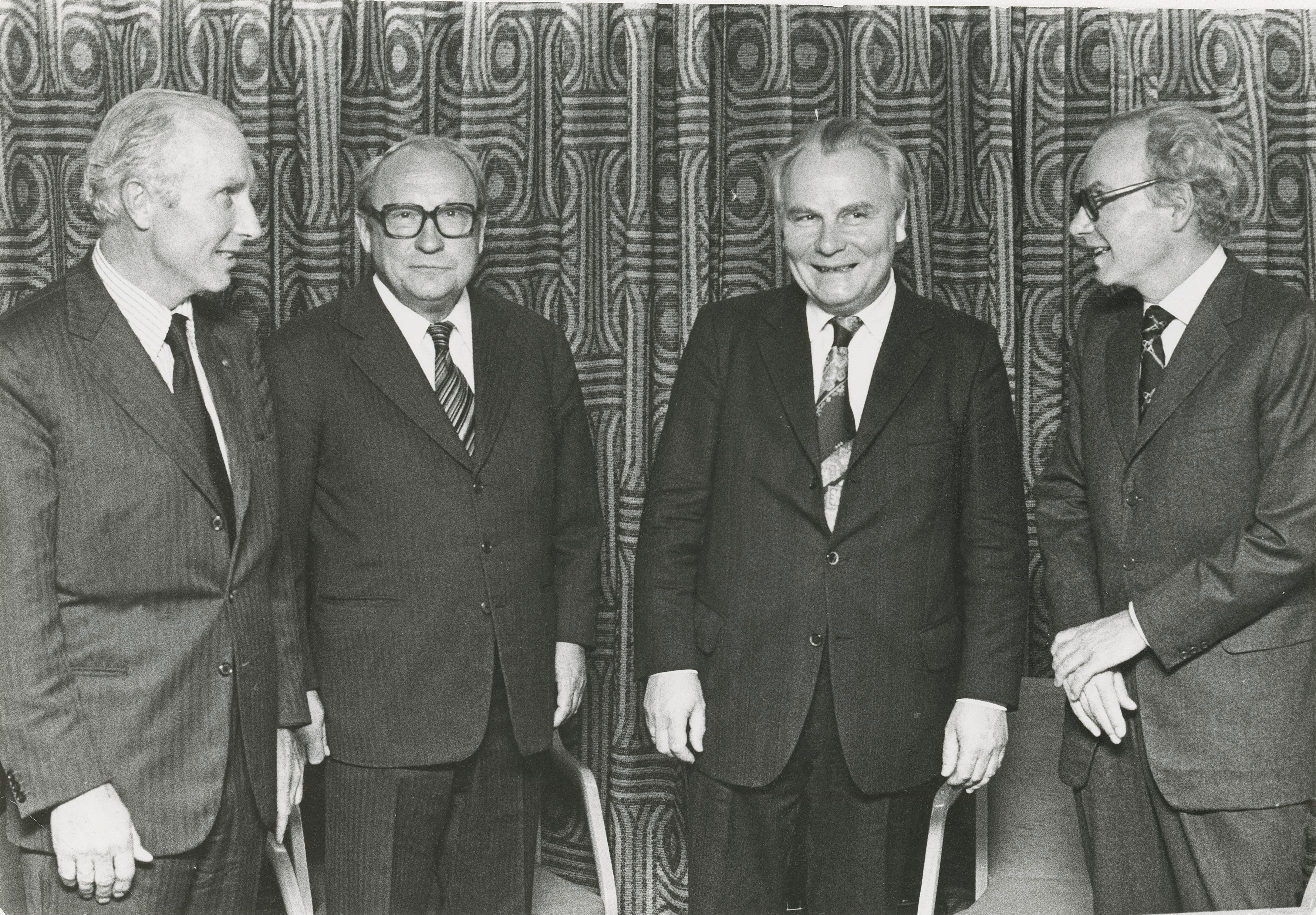 Bildet viser fire litt eldre menn i dress som står ved siden av hverandre. De smiler og ser glade ut. 