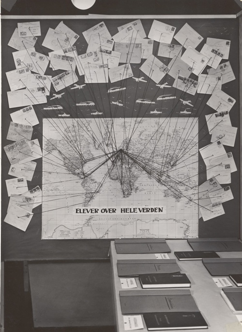 Et bilde av en verdenskart hvor det er festet mange postkort rundt til ulike steder i verden.