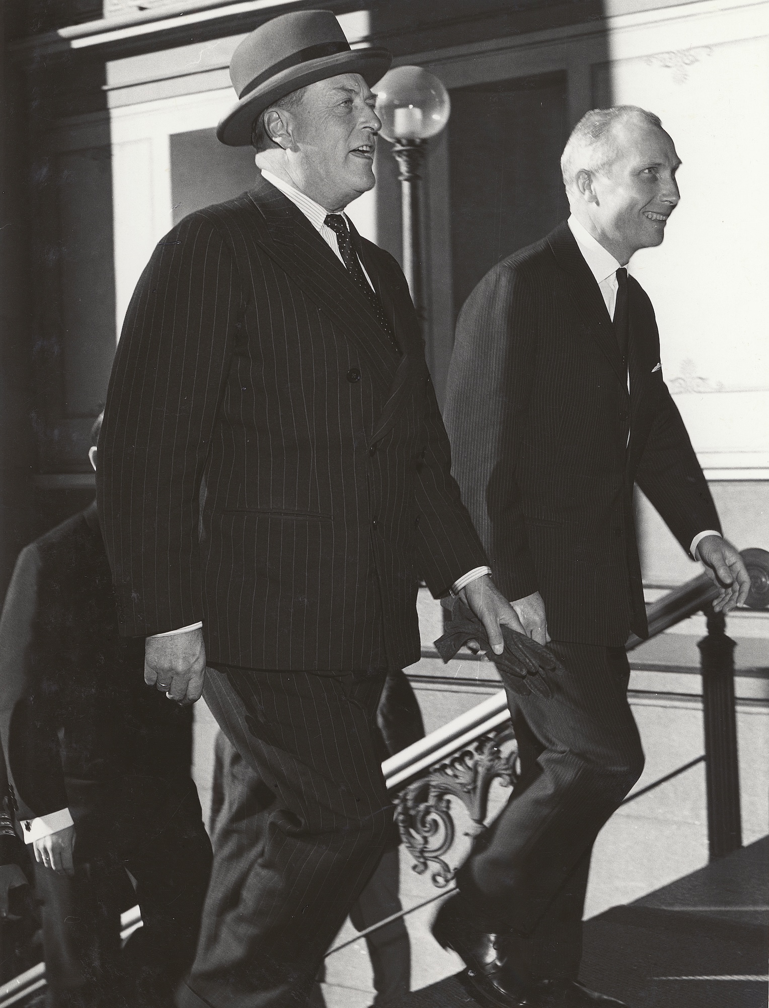 To menn i dress smiler og går opp over en trapp