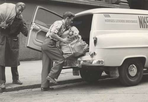 To menn med 50-års hårssveis bærer sekker med post inn i en postbil. 