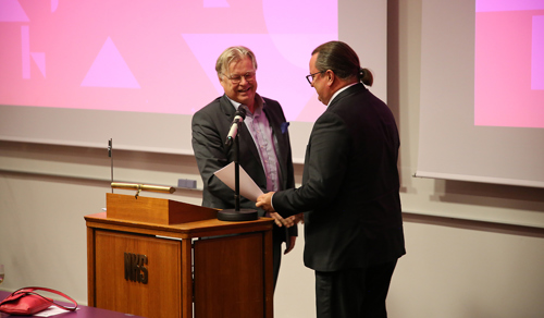 To menn i dress står sammen bak en talerstol. 