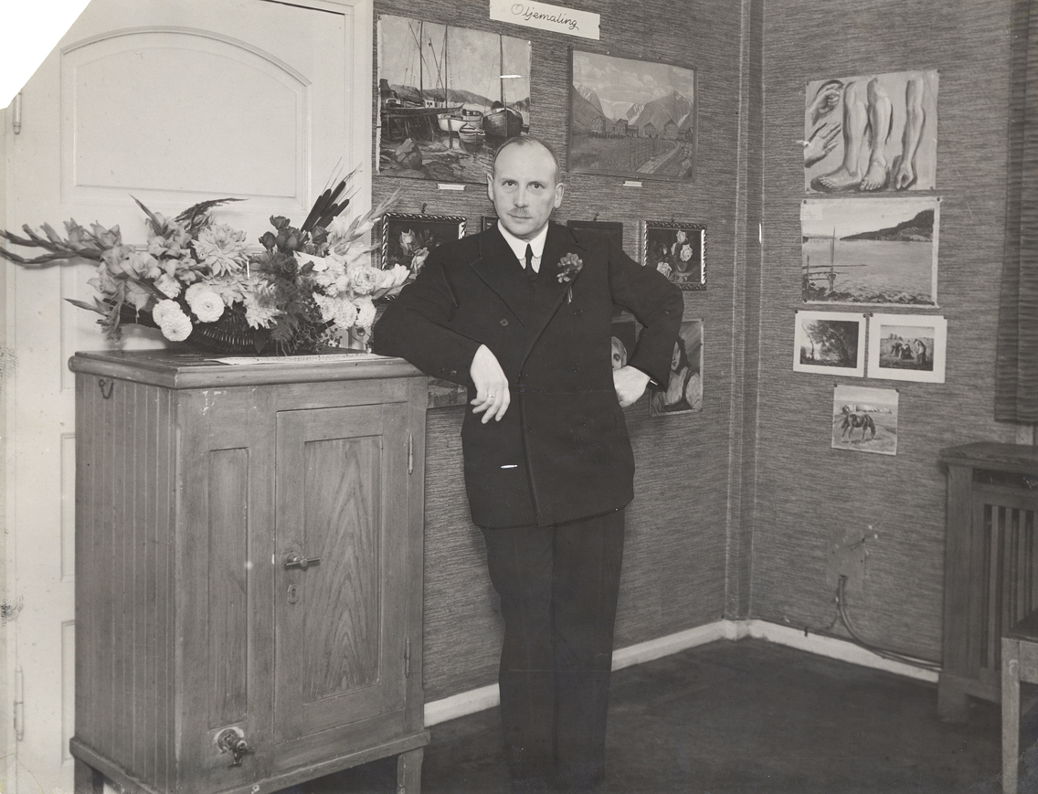 En ung mann i dress står ved siden av et isskap i tre.