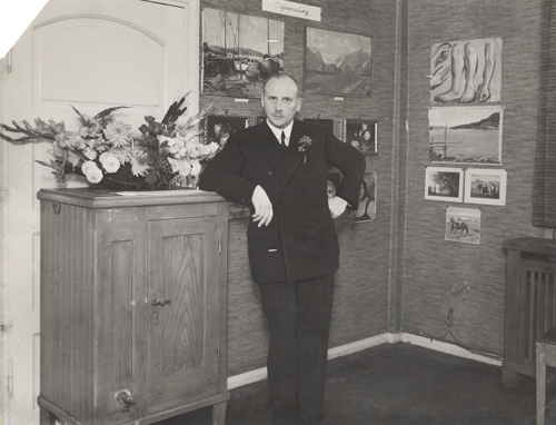 En ung mann i dress står ved siden av et isskap i tre.