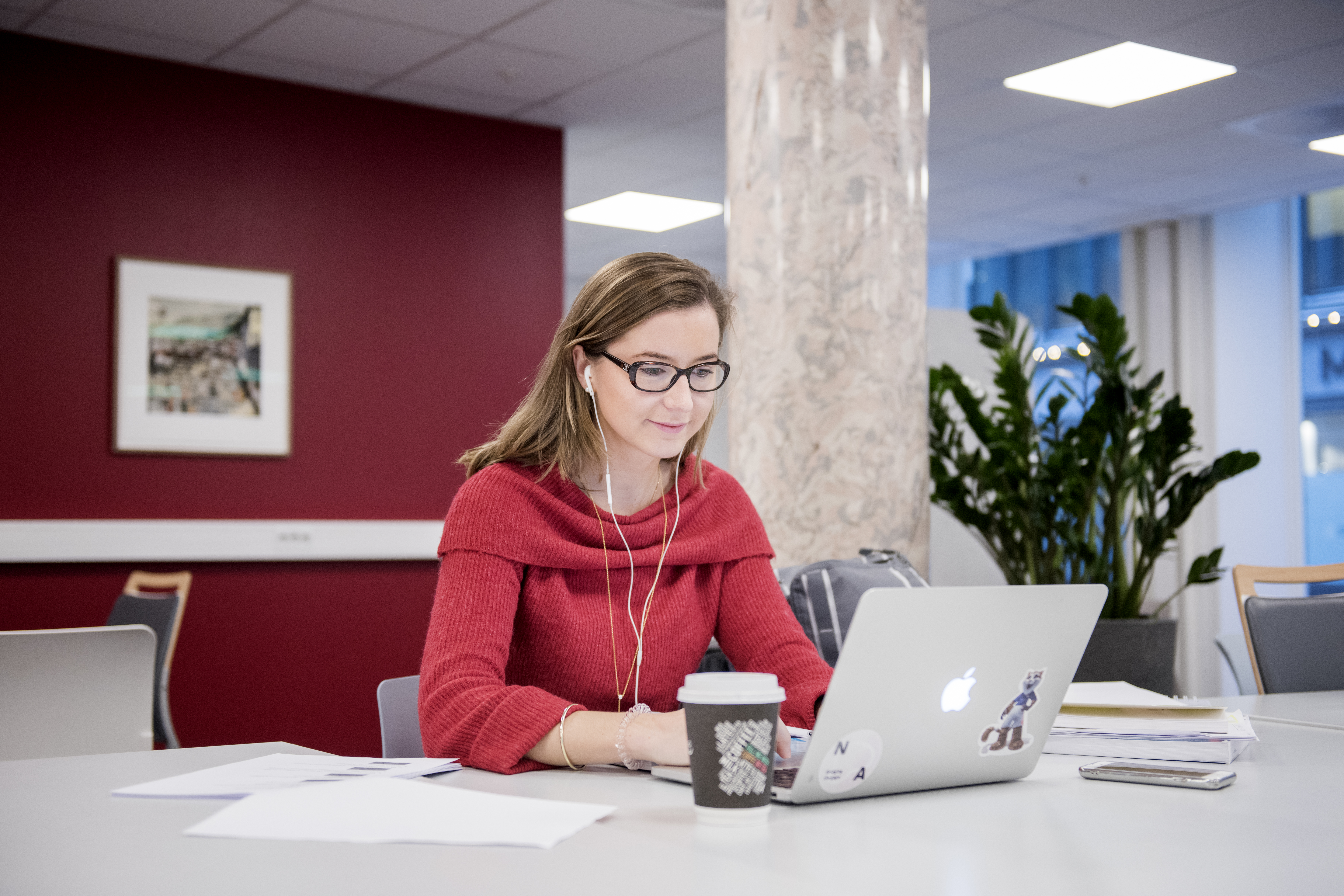 Foto av kvinnelig student som sitter med laptop i et kontorlokale.
