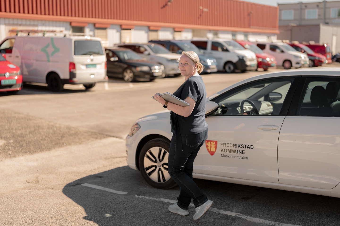 Tidligere nettstudent med PC i hånden går ved siden av tjenestebil på en parkeringsplass.