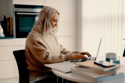 Genette Våge som sitter på laptopen sin på kjøkkenet