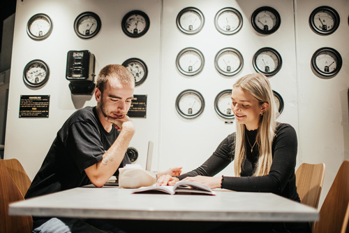Foto av kvinnelig og mannlig student ved et bord som ser i en bok sammen.